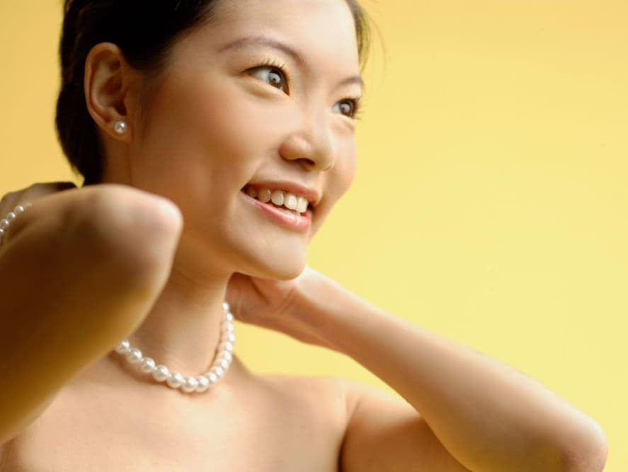 woman putting on pearl necklace