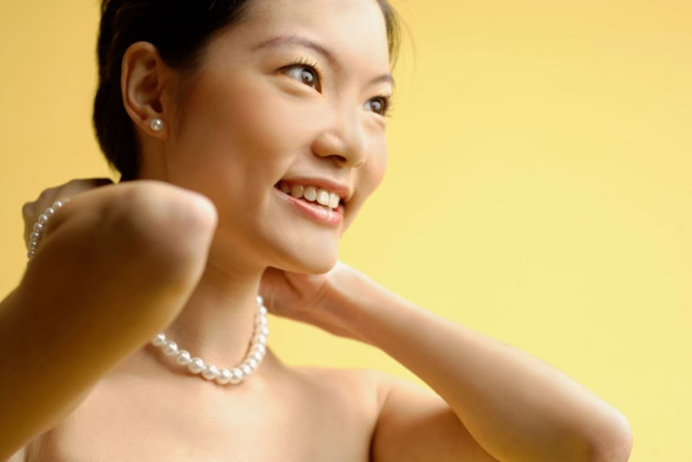 woman putting on pearl necklace 